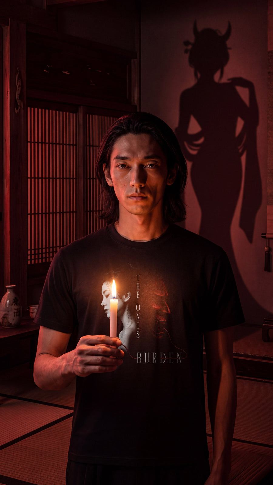 Oni’s Burden t-shirt, editorial photograph — a red-lit room, a candle, and the oni's shadow on the wall